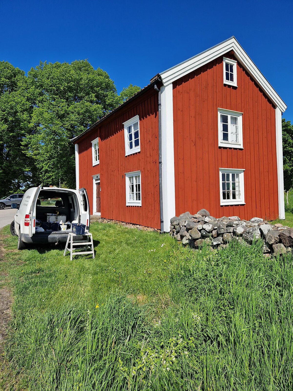 Rödmålat tvåvåningshus med vita knutar och spröjsade fönster
