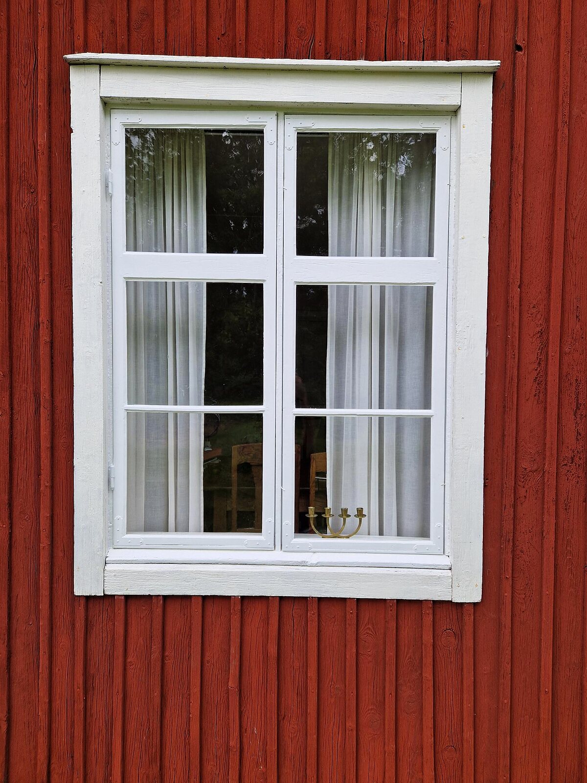Vitmålat spröjsat fönster i röd träpanel